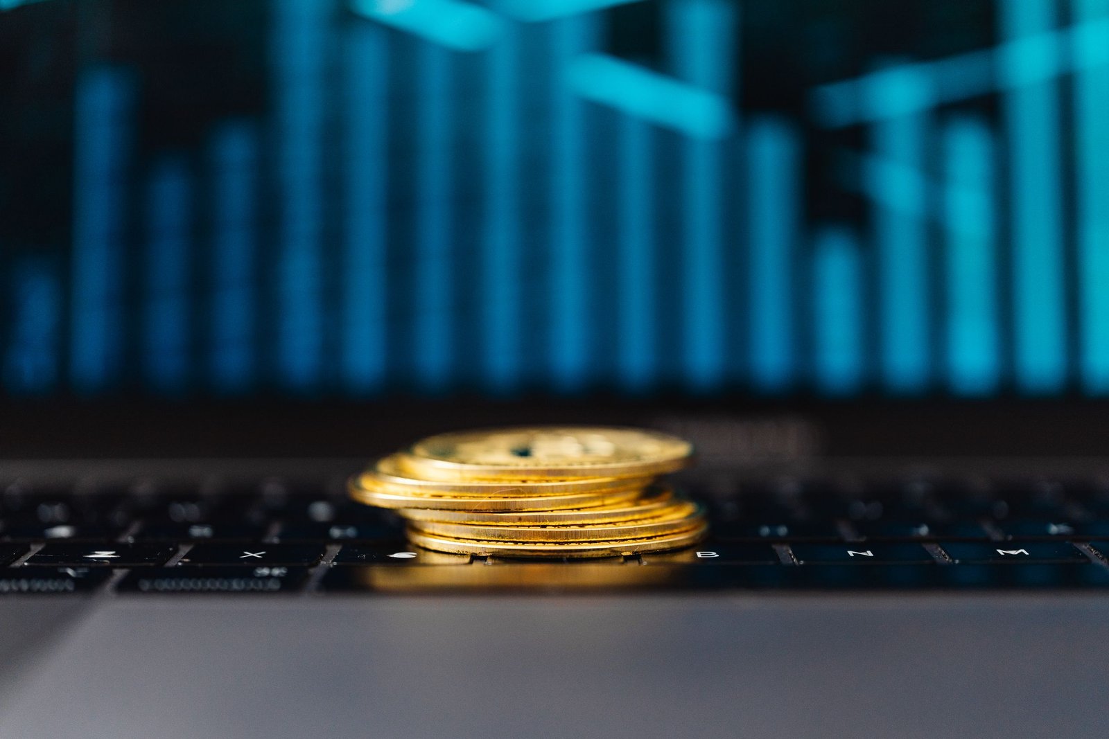 Stack of gold coins on a laptop keyboard beside a rising graph